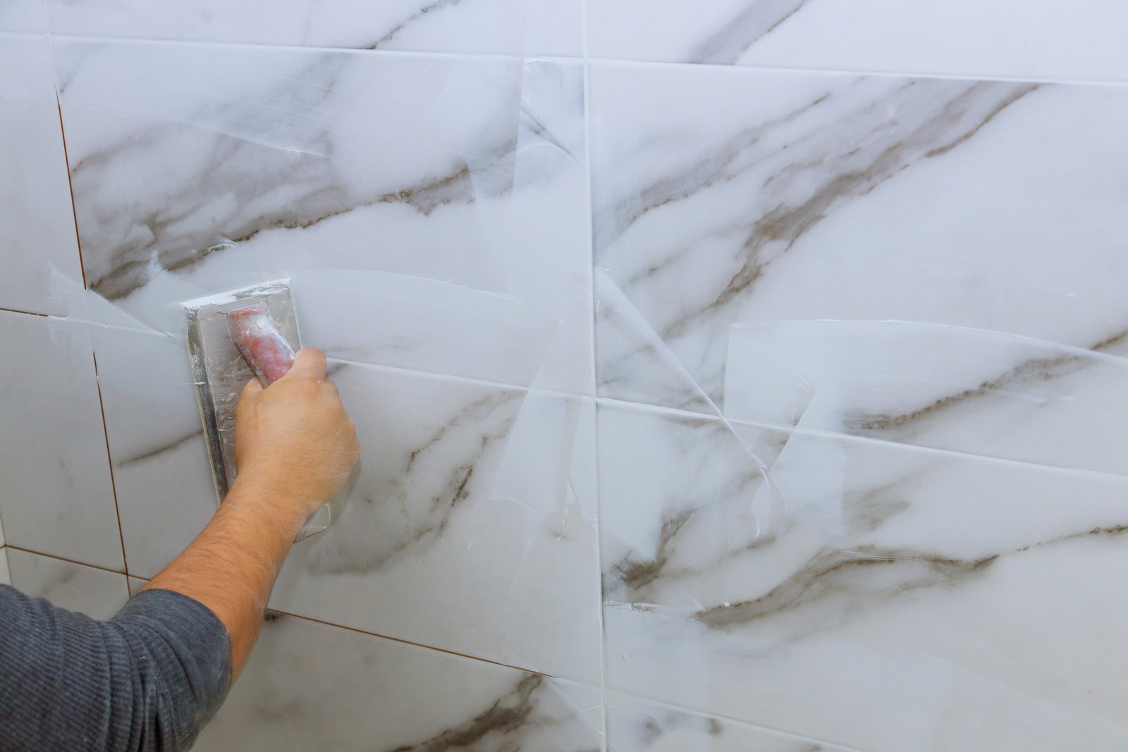 Worker applying cementitious grout between ceramic tiles