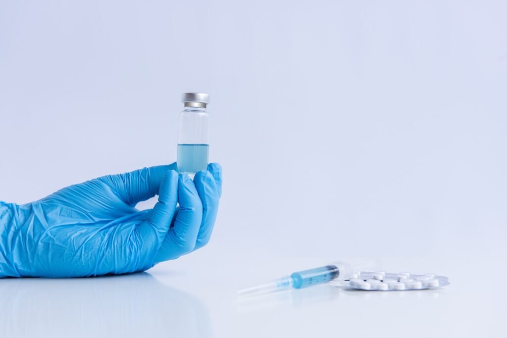 On white isolated background, hands of doctor in medical blue gloves hold ampoule vaccine