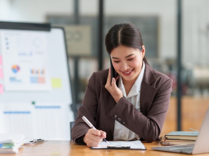 Professional asian business woman sitting working and talking on the phone while with a laptop